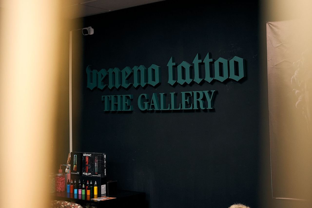 Cartel de entrada donde se lee 'Veneno Tattoo The Gallery' en un estudio de tatuajes
